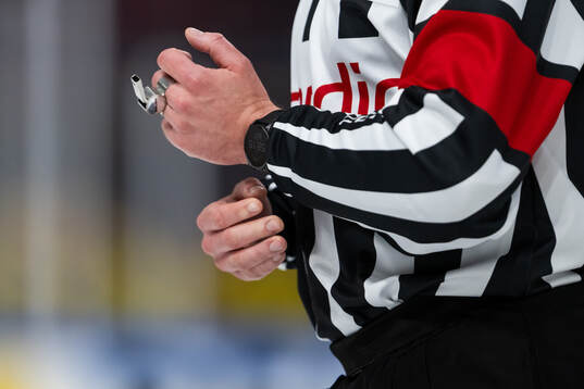 A hand of a referee holds a whistle