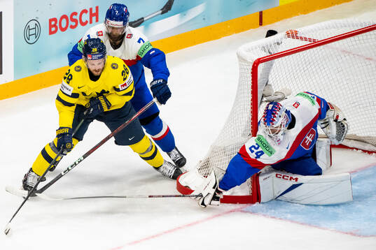 Elias Lindholm of Sweden competes for the puck with Mario