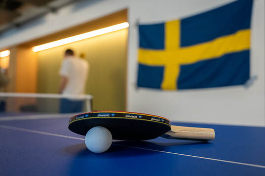 A Table Tennis racket and ball with a Swedish flag behind