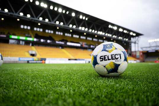 Select fotboll på konstgräset med läktare i bakgrunden