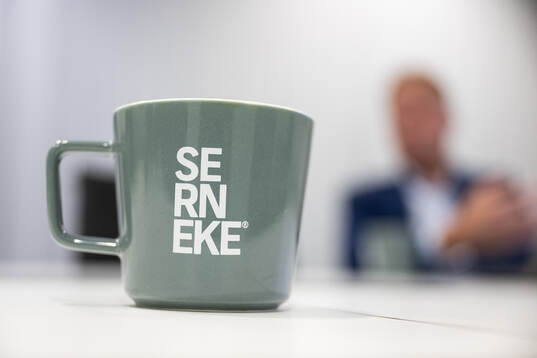 En kaffemugg med texten Serneke och i bakgrunden syns Ola