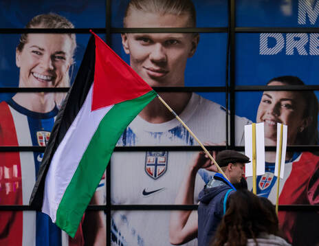 A Palestinian protester walks past a collage showing